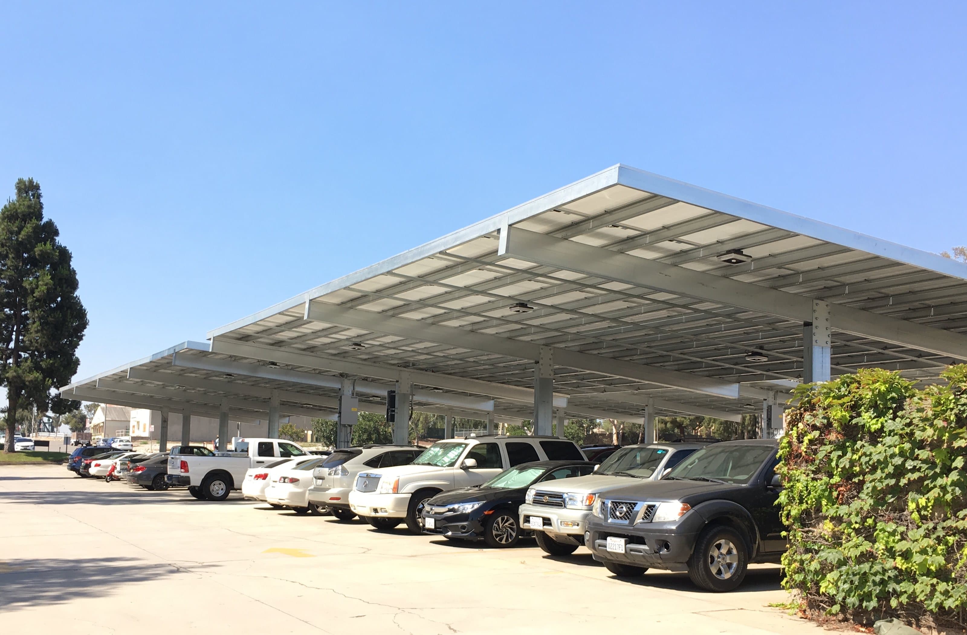Row of semi-cantilever solar carports over dealership parking on a clear day